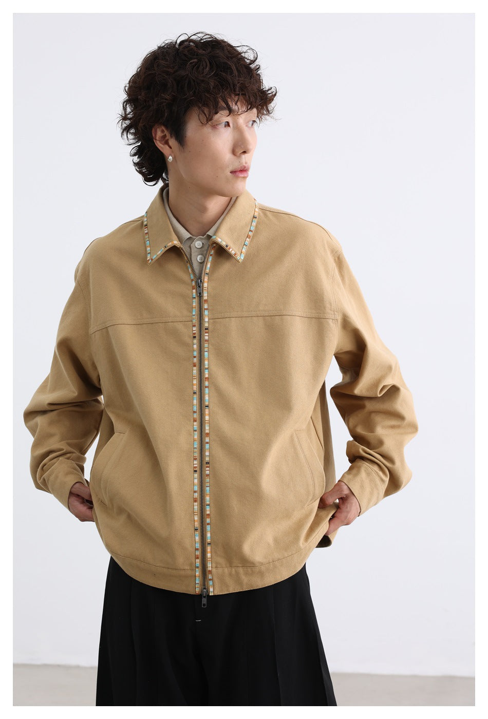 Model wearing a tan zip-front jacket with multicolor trim along the collar and zipper, shown from the front.