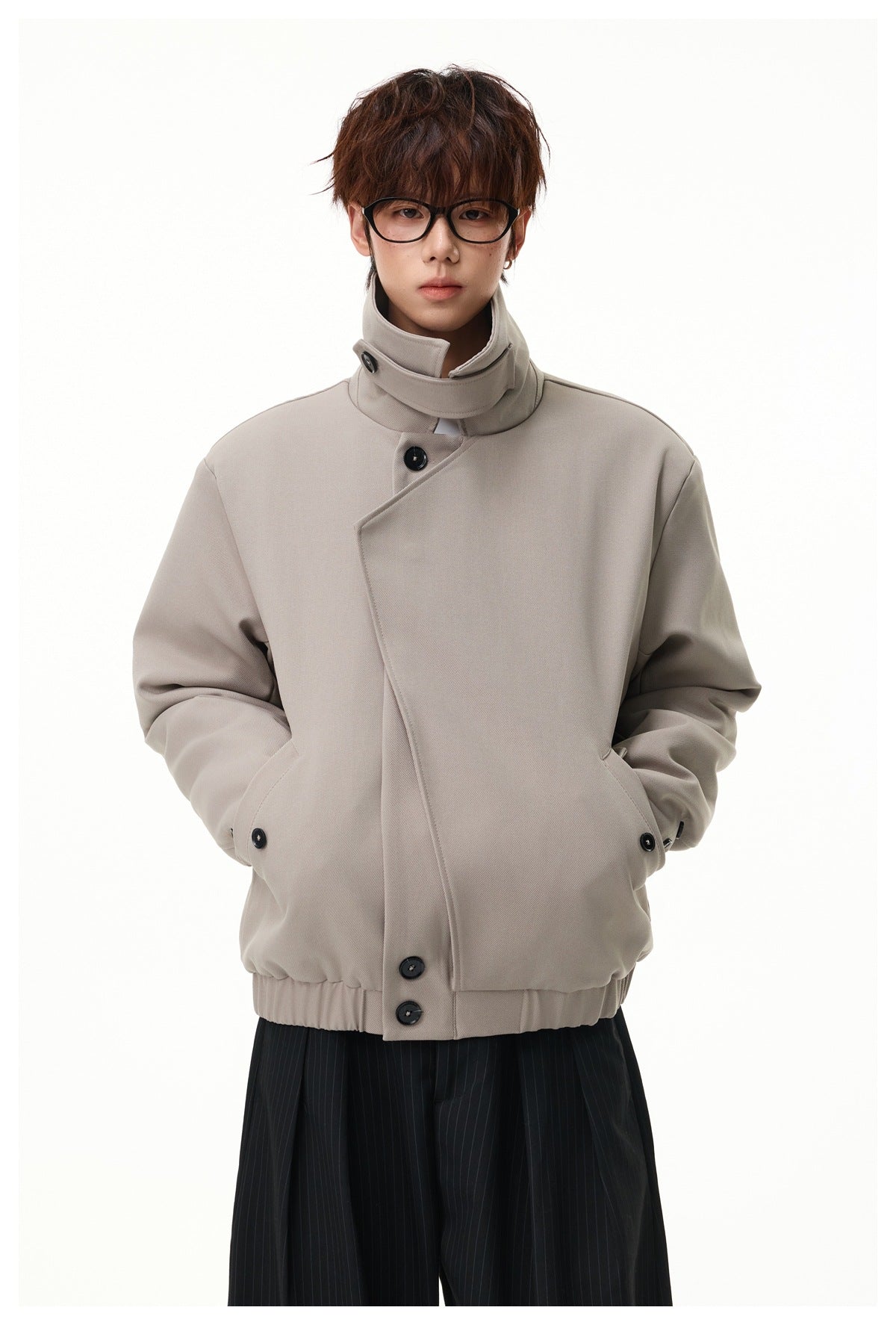 Model wearing a taupe jacket with a tall collar, asymmetrical button front, and gathered hem.
