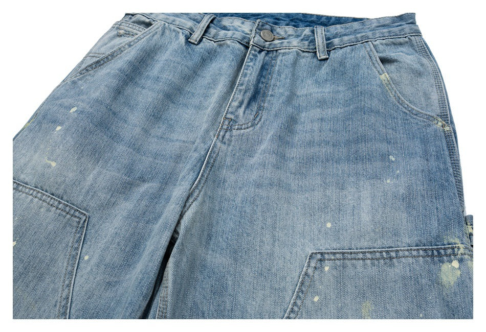 Upper front view of light blue jeans with a button waist, front pockets, large utility pockets and distressed marks.
