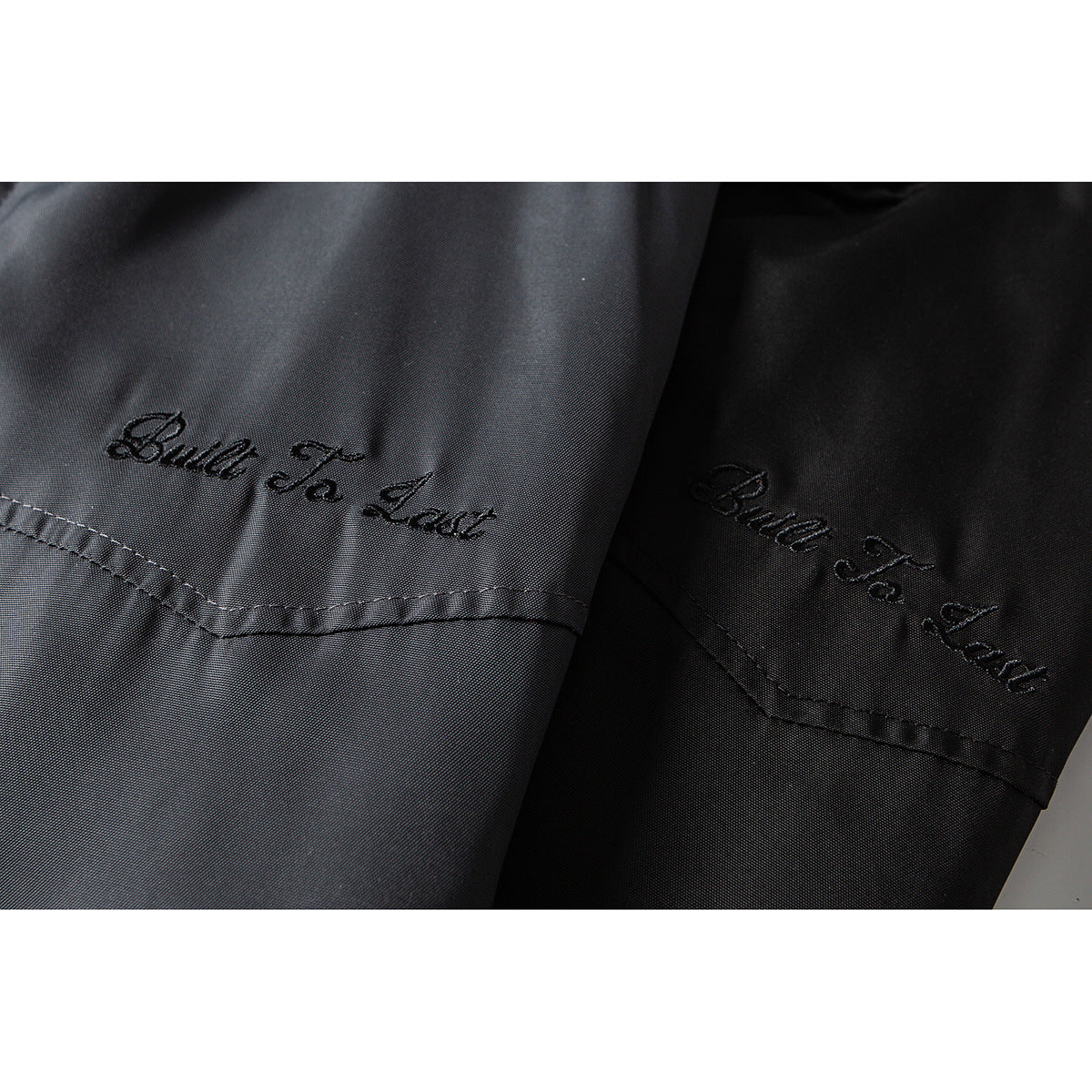 Close-up of gray and black jacket panels with embroidered “Built To Last” lettering.