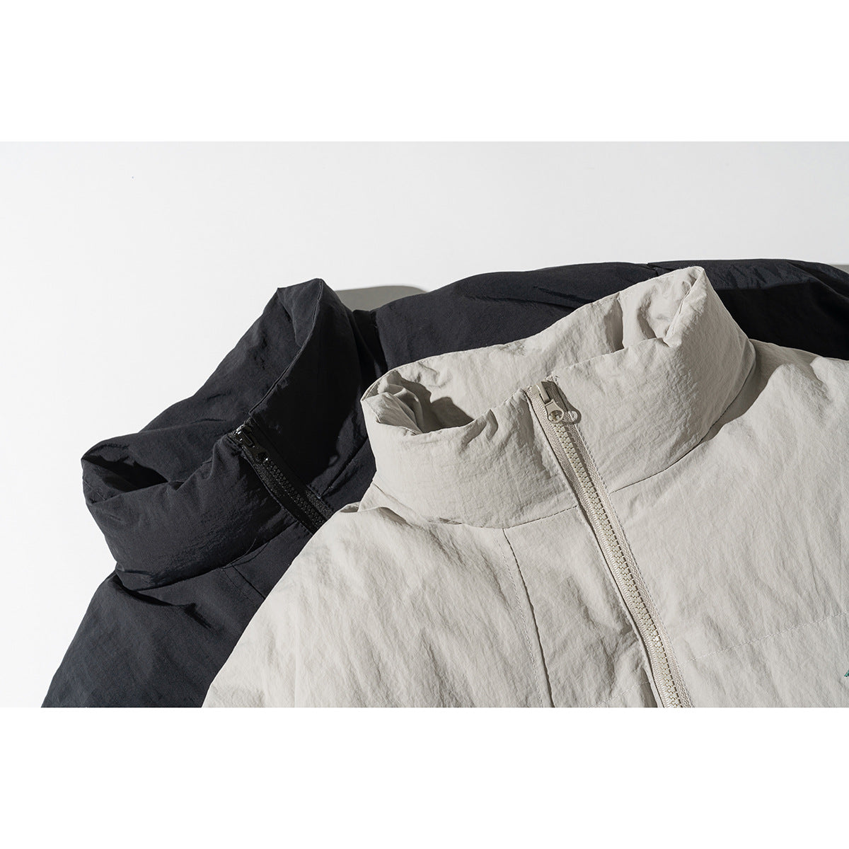 Close-up of black and light beige padded jackets showing their high collars and front zippers.