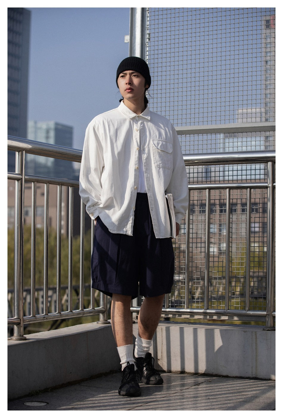 Model wearing loose navy shorts with a white button-front shirt and chest pocket.