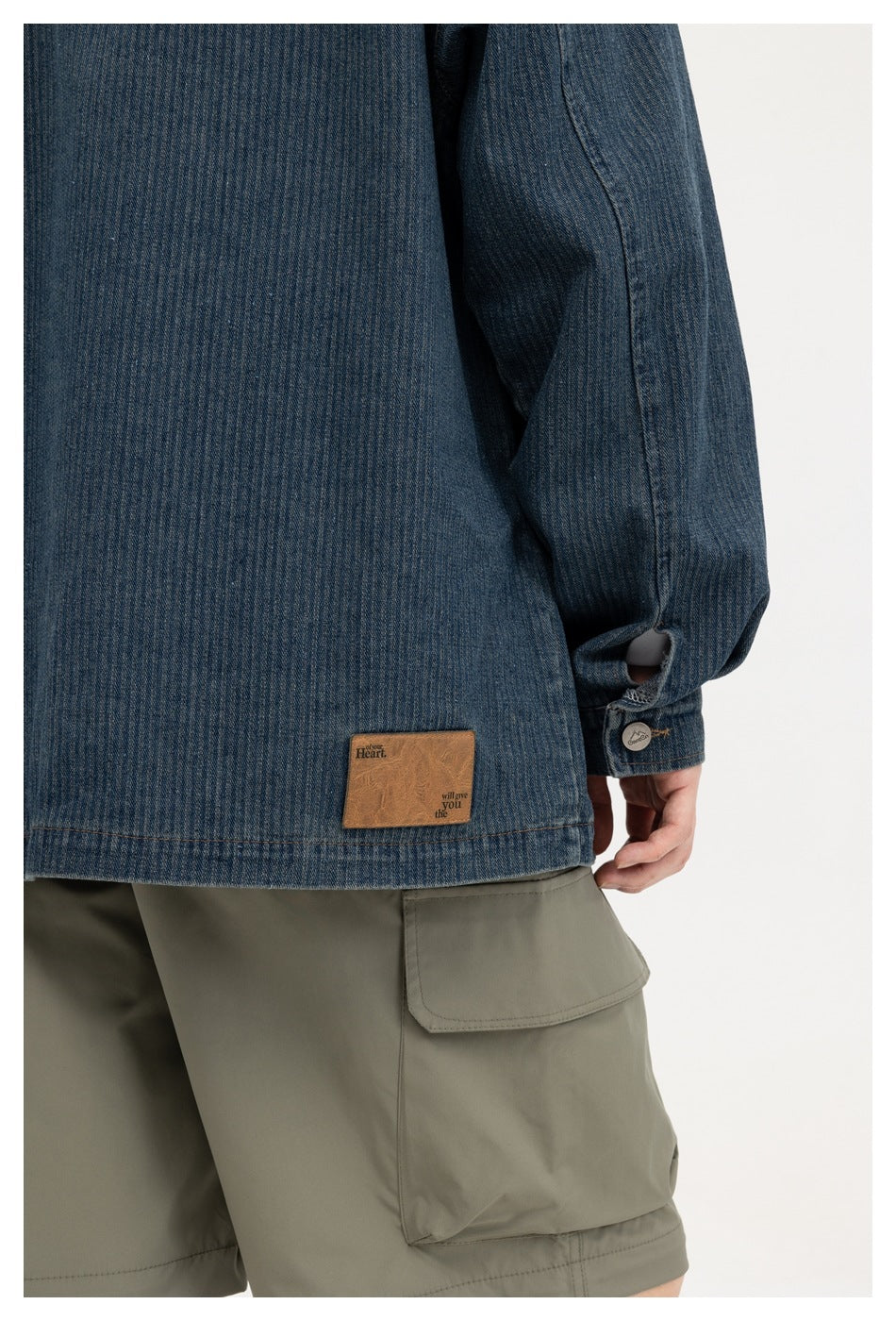 Close-up of the jacket's dark blue denim back hem, sleeve cuff, and small brown patch.