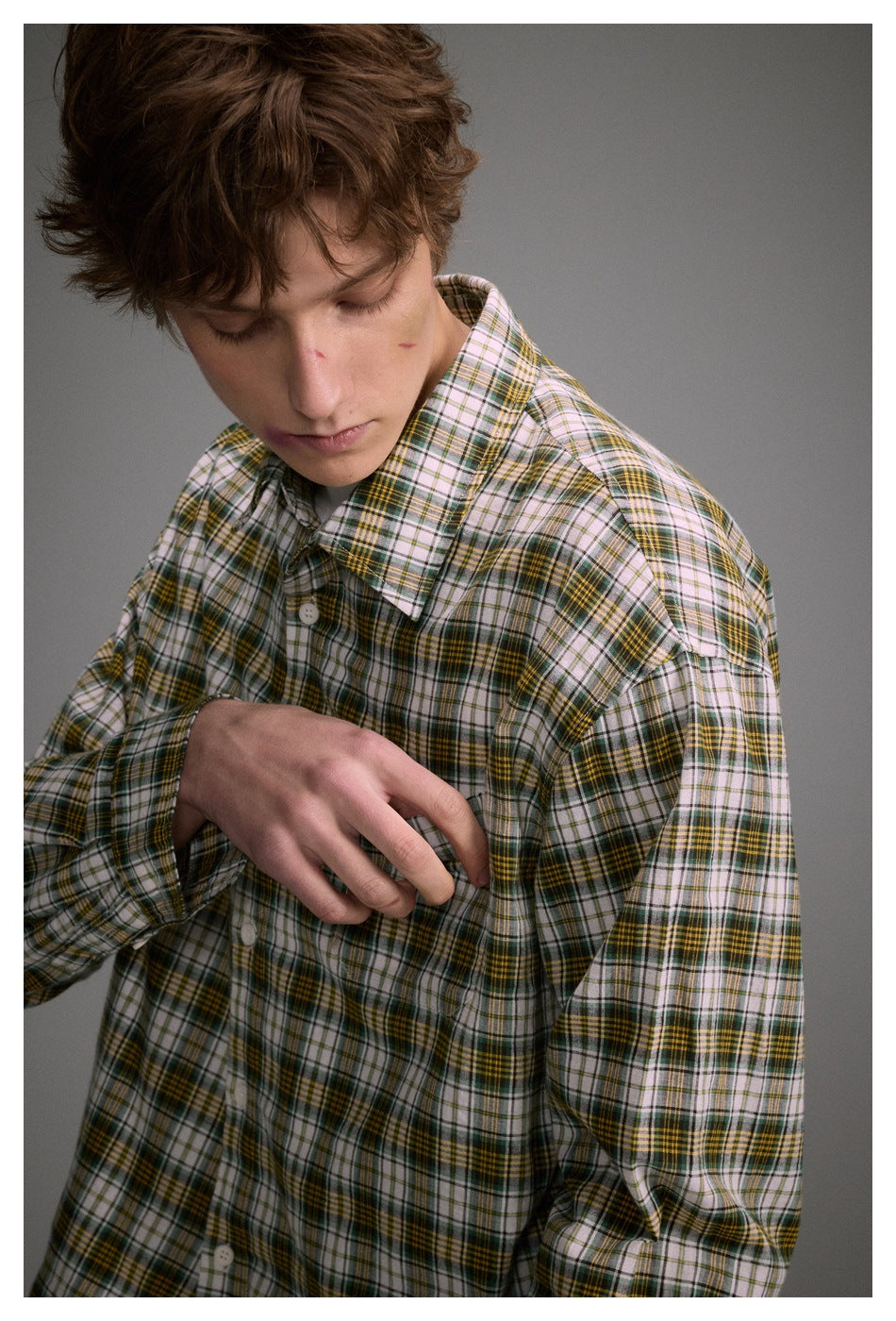 Close-up of a model wearing a white, green, and mustard plaid button-up shirt, showing its collar and sleeve.