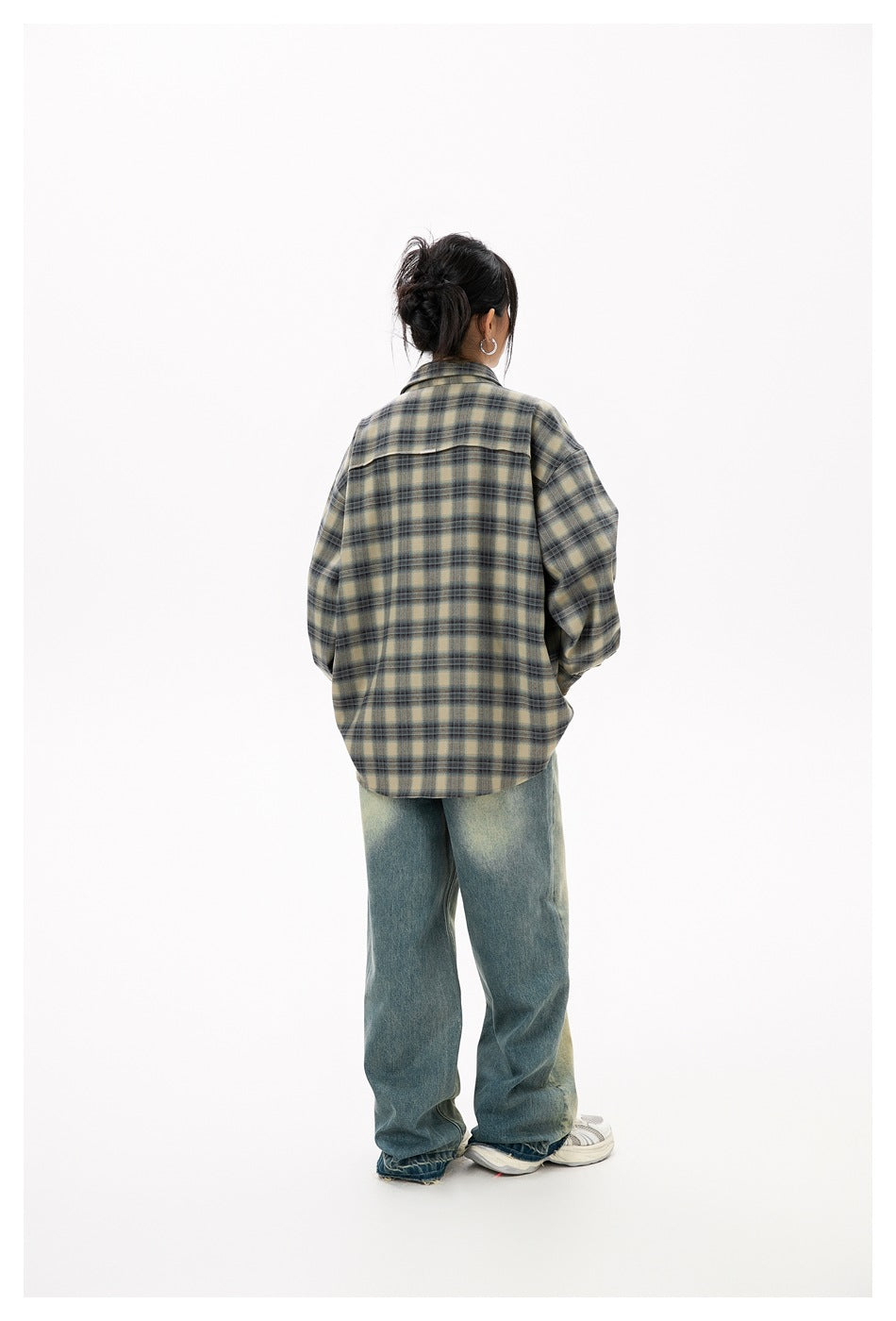 Back view of a model wearing an oversized olive and blue plaid shirt and loose blue jeans.