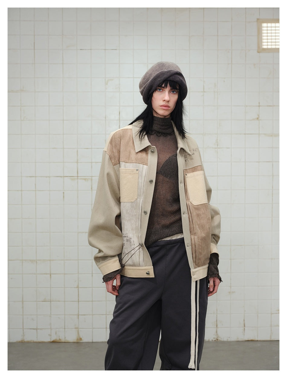 Model wearing an open neutral patchwork jacket over a dark mesh top and loose black trousers.