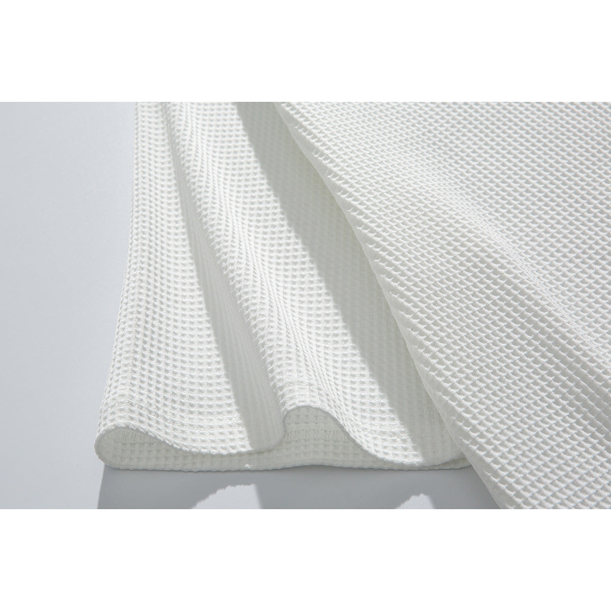 Close-up of the hem and draped panels of a white waffle-textured shirt.