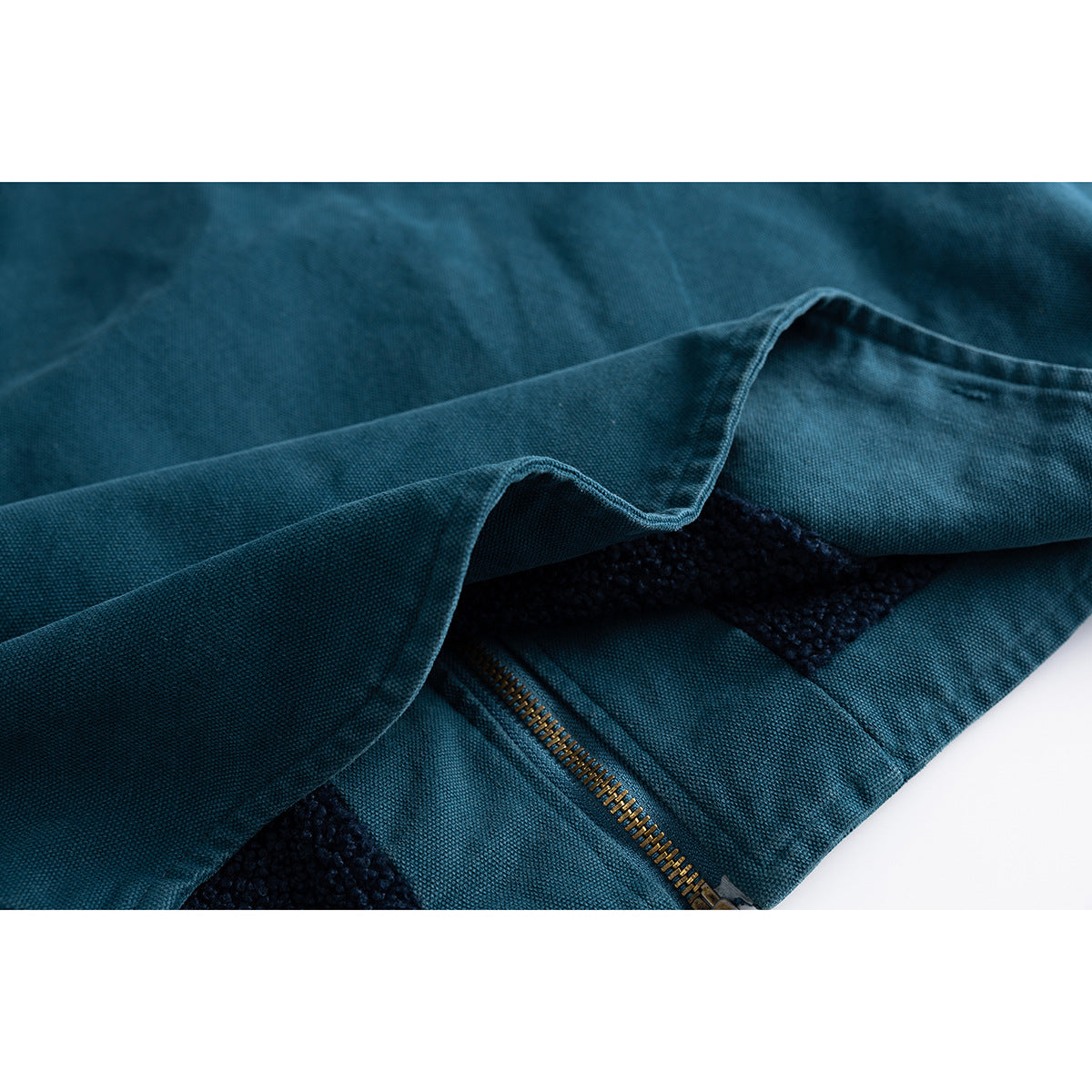 Close-up of teal vest fabric folded back to show dark textured lining, stitching and zipper teeth.