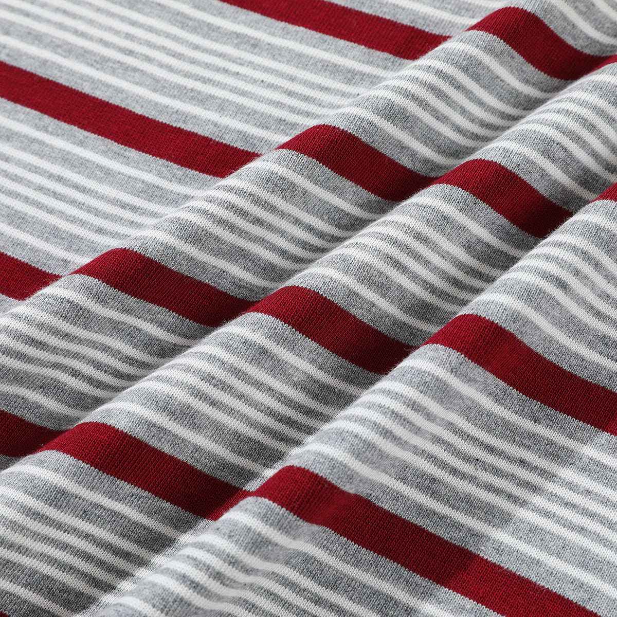 Close-up of gray-and-white knit fabric with broad burgundy stripes, softly draped in folds.