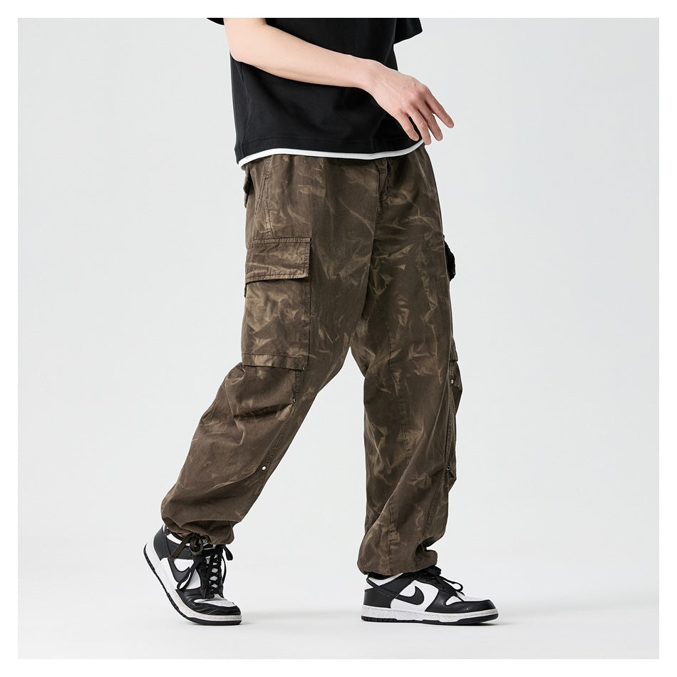 Side view of a model walking in coffee brown tie-dye cargo pants with flap pockets and gathered cuffs