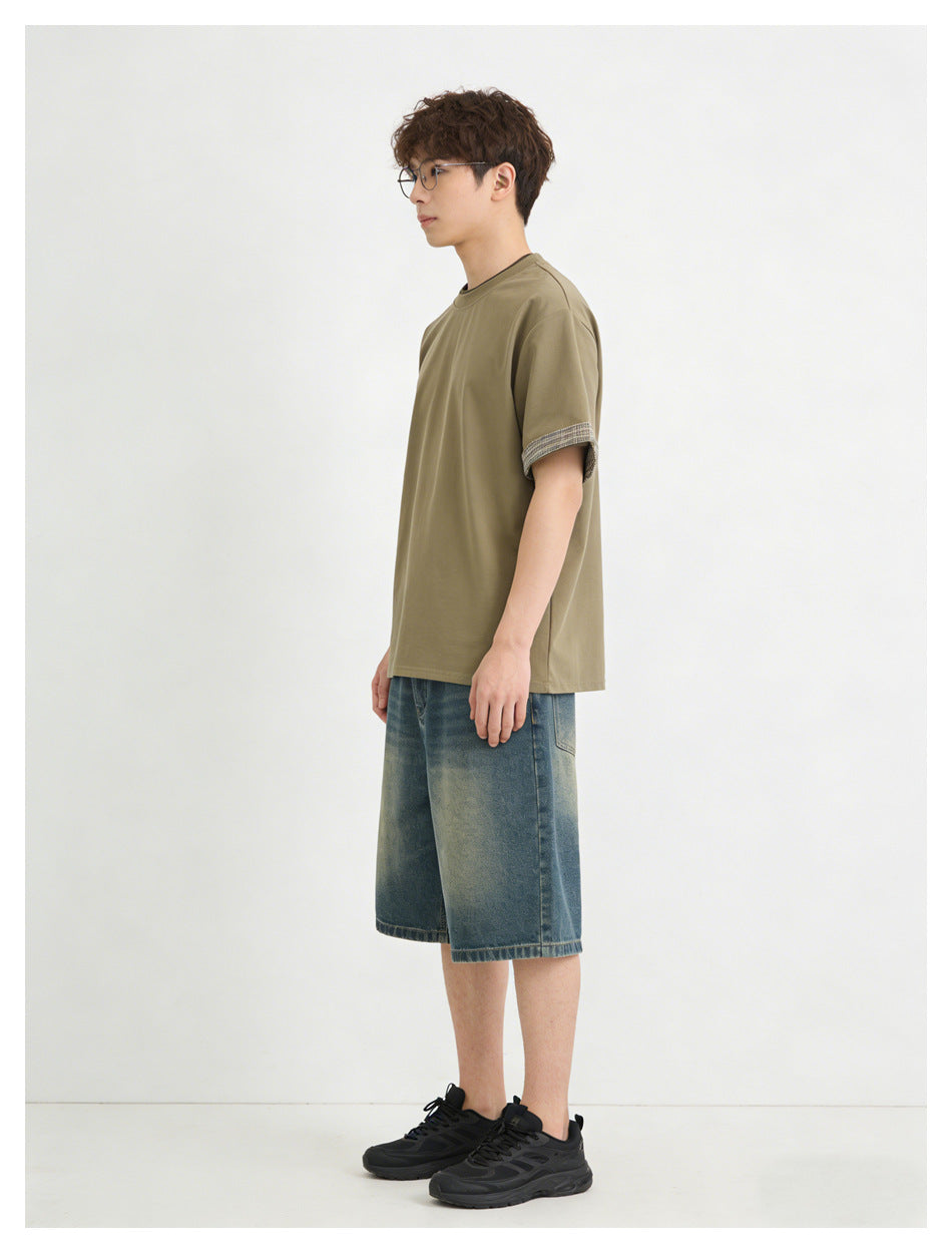 Side view of a model wearing an olive-brown short-sleeve T-shirt with patterned cuff trim and denim shorts.