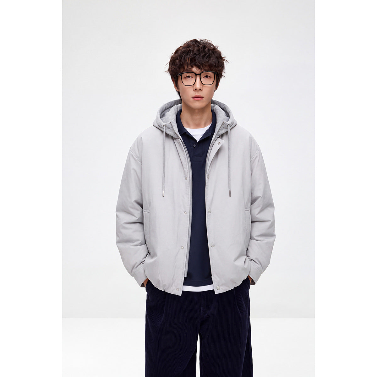 Front view of a model wearing a light gray hooded jacket with drawstrings, snaps, and front pockets.