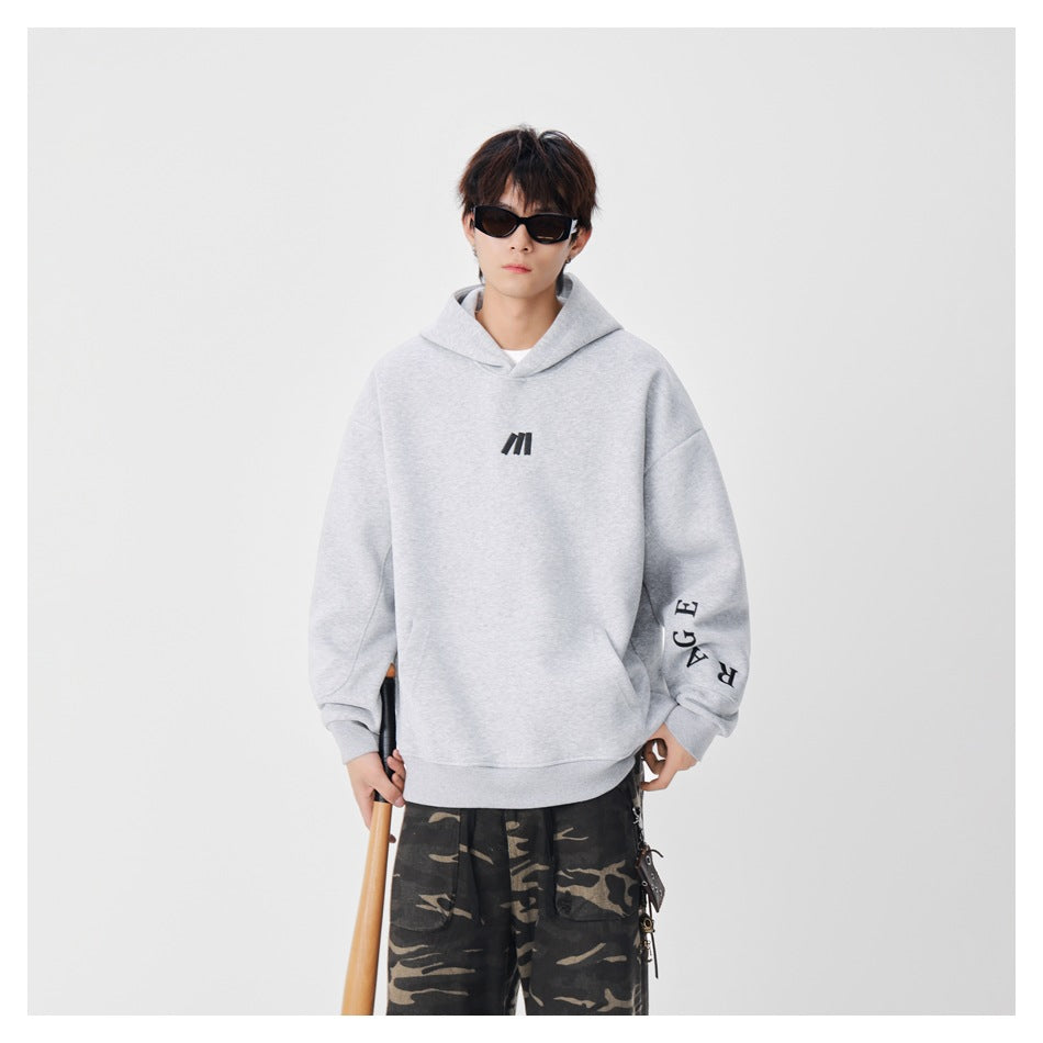 Front view of a model wearing a light gray oversized hoodie with a black chest mark and lettering on one sleeve.
