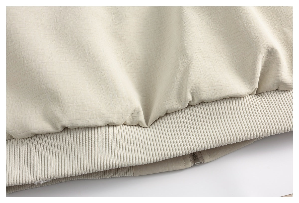 Close-up of the cream jacket's textured fabric, ribbed hem, and partially visible zipper.