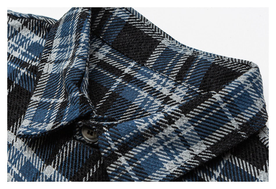 Close-up of the pointed collar and button on blue, black, and white plaid shirt fabric.