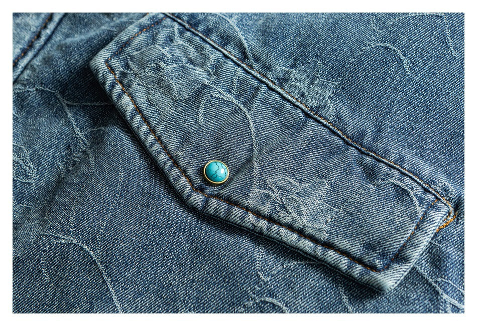 Close-up of a blue denim flap pocket with orange stitching and a round turquoise button.