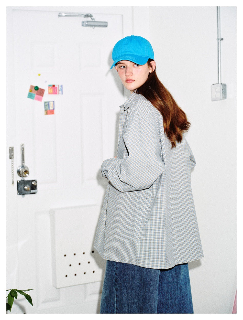 Side and back view of a model wearing an oversized gray-blue plaid shirt, jeans, and a bright blue cap.