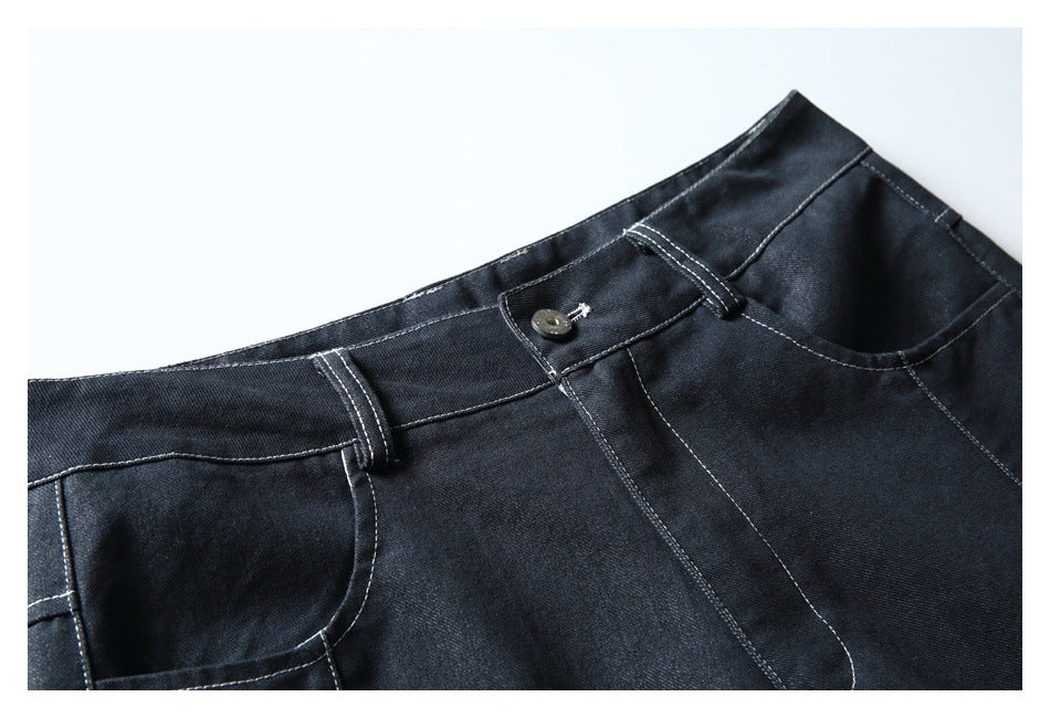 Close-up of dark indigo trousers showing the waistband, button, belt loops, and curved front pockets.