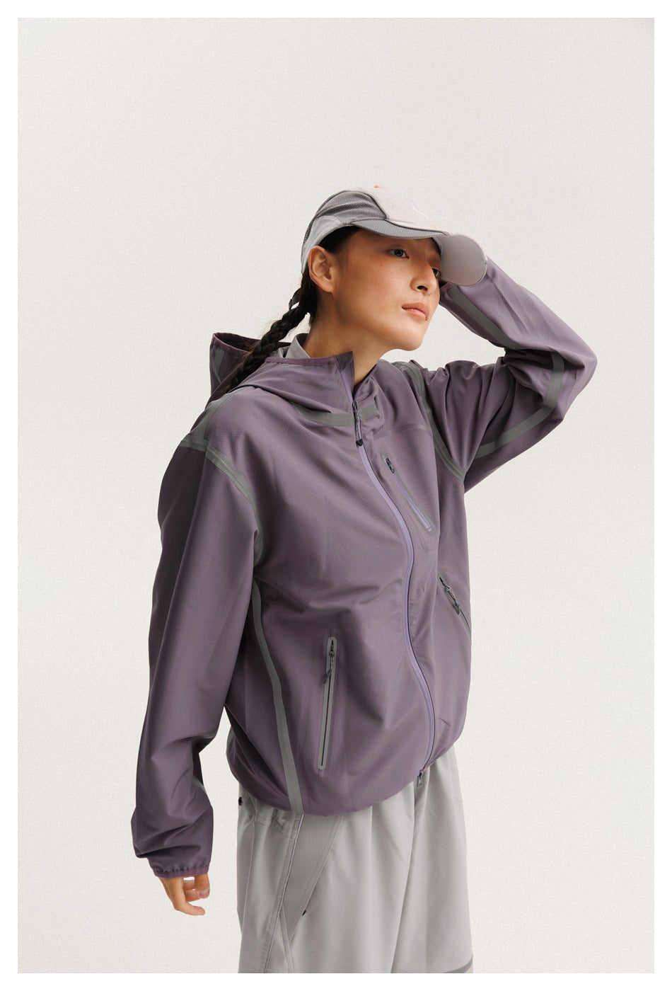 Closer view of a model wearing a muted purple hooded jacket with zip pockets and light gray pants.
