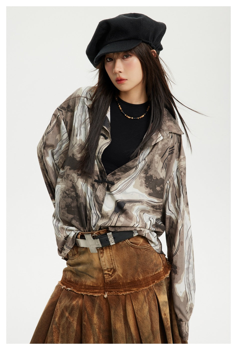 Close-up of a model wearing the coffee ink-print shirt with frog button, black top, beret and cross belt buckle