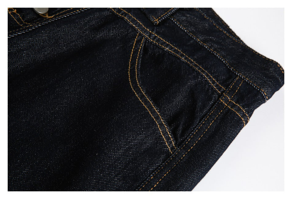 Close-up of a curved front pocket and contrast stitching on dark indigo jeans.