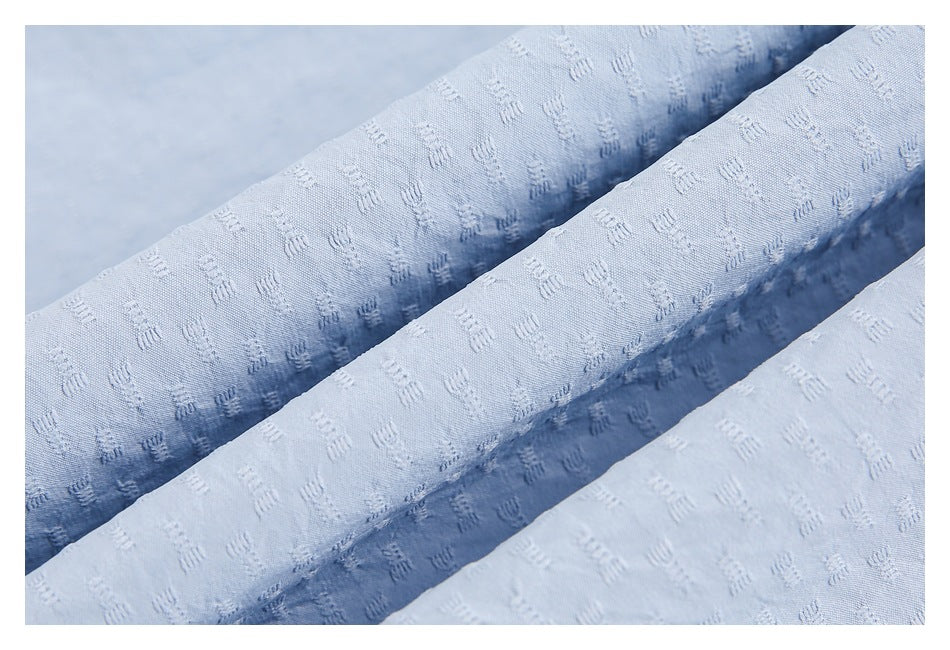 Close-up of pale blue shirt fabric gathered into folds, highlighting its subtle textured pattern.