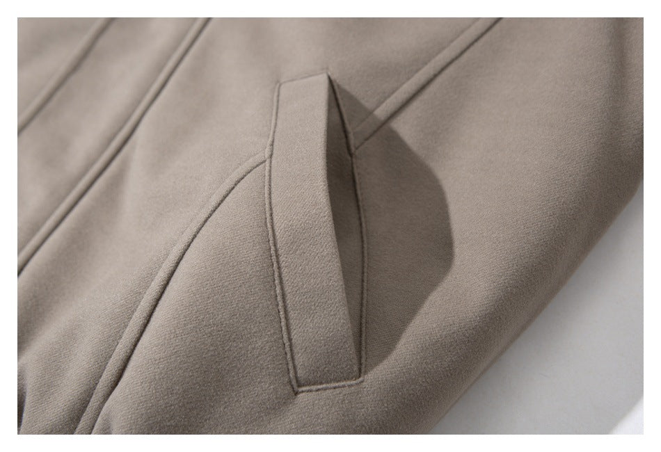 Close-up of a taupe jacket pocket with a narrow fabric flap and curved seam.