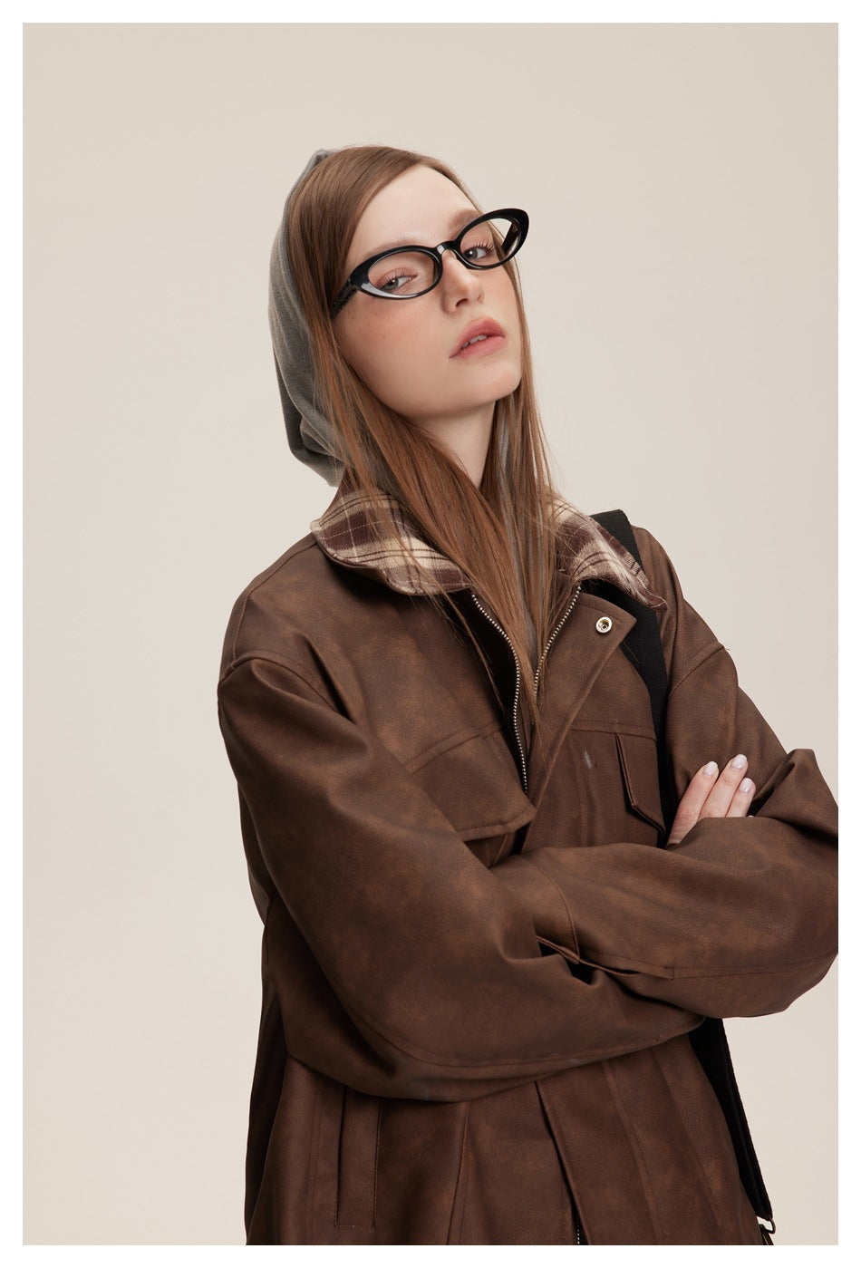 Close view of a model wearing an oversized brown jacket with plaid collar, gray hood and flap pockets.