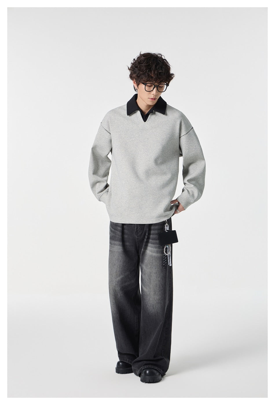 Front view of a model in a light gray pullover with a black collar and stitched shoulder details.