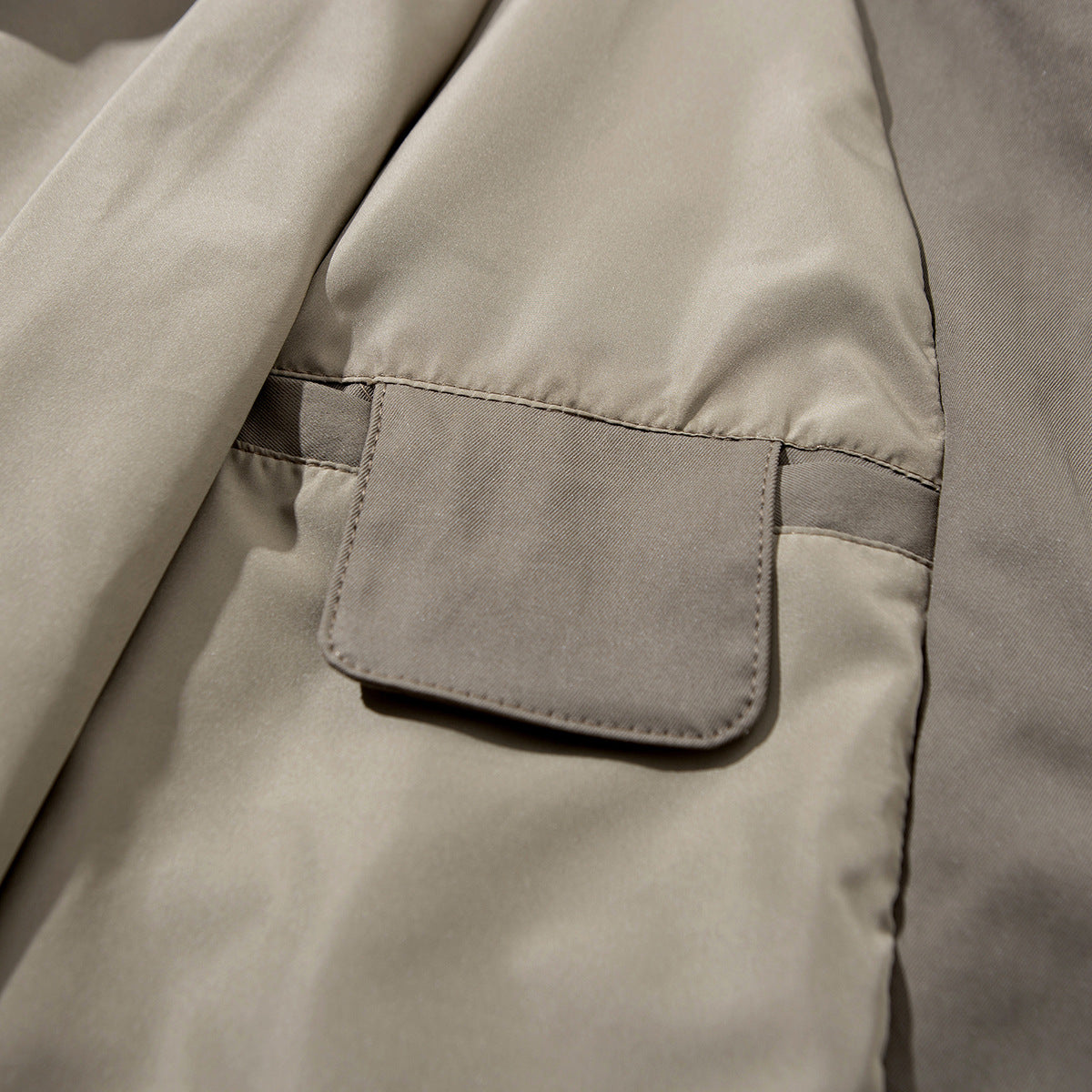 Close-up of a taupe jacket's rectangular pocket flap and interior construction.