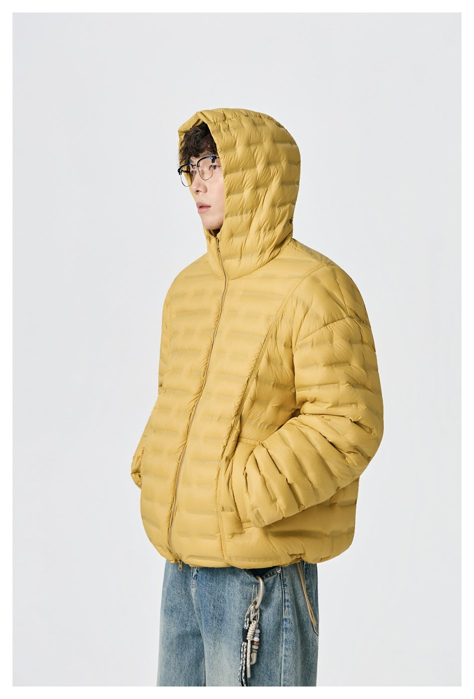 Three-quarter view of a model in a zipped mustard-yellow hooded quilted jacket with hands in the pockets.