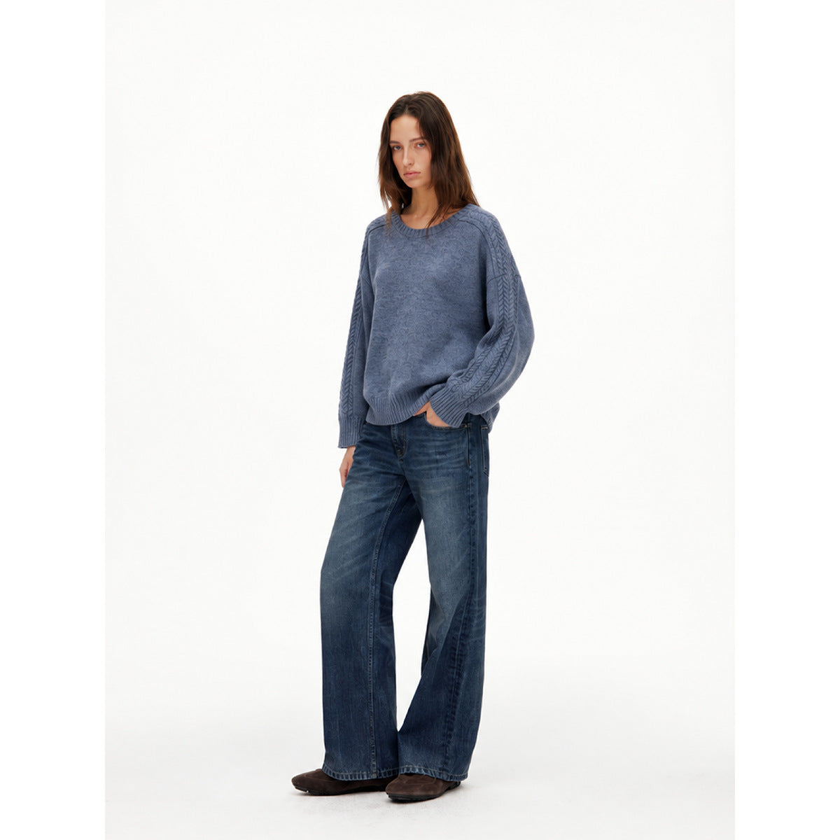 Model wearing a blue-gray crewneck sweater with cable-knit sleeve panels and ribbed cuffs, hem, and neckline.