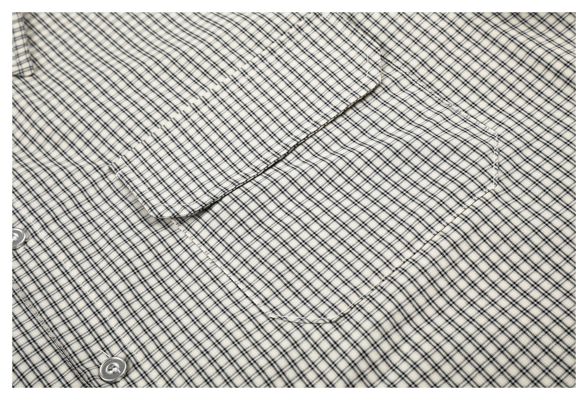 Close-up of a cream shirt with a black plaid pattern, showing a chest pocket and buttons.