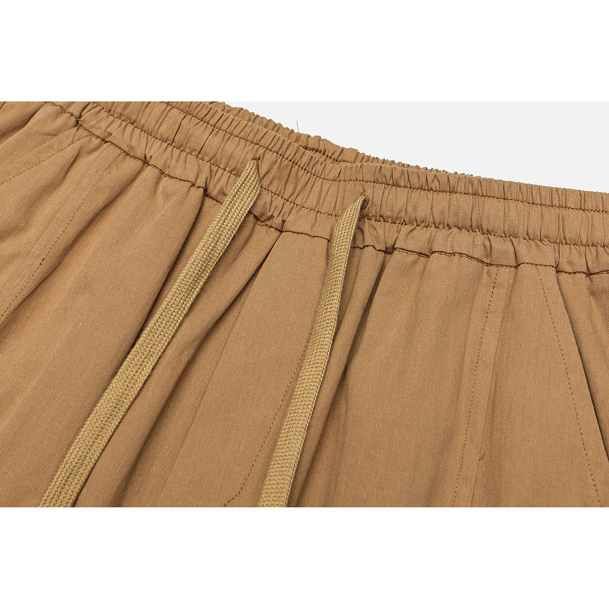 Close-up of tan shorts showing the elastic waistband, braided drawstrings, stitching and pleated fabric.