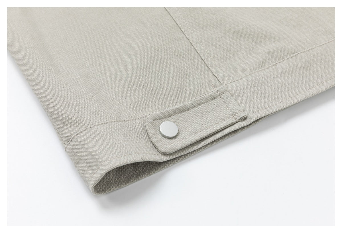 Close-up of a light beige garment cuff with a stitched snap-button tab and seam.