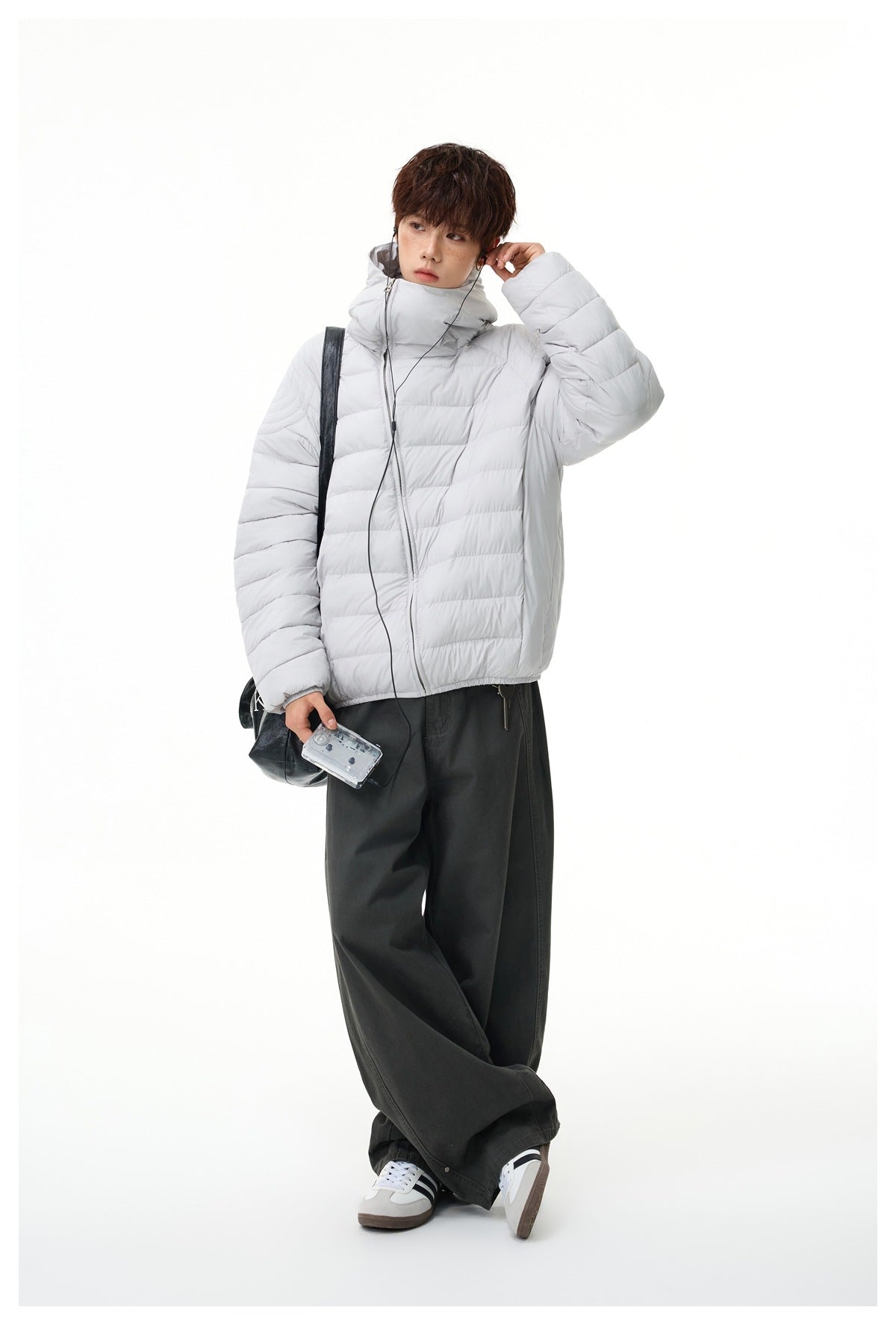 Full-length view of model in light gray hooded quilted jacket, wide dark gray pants and sneakers with a black shoulder bag