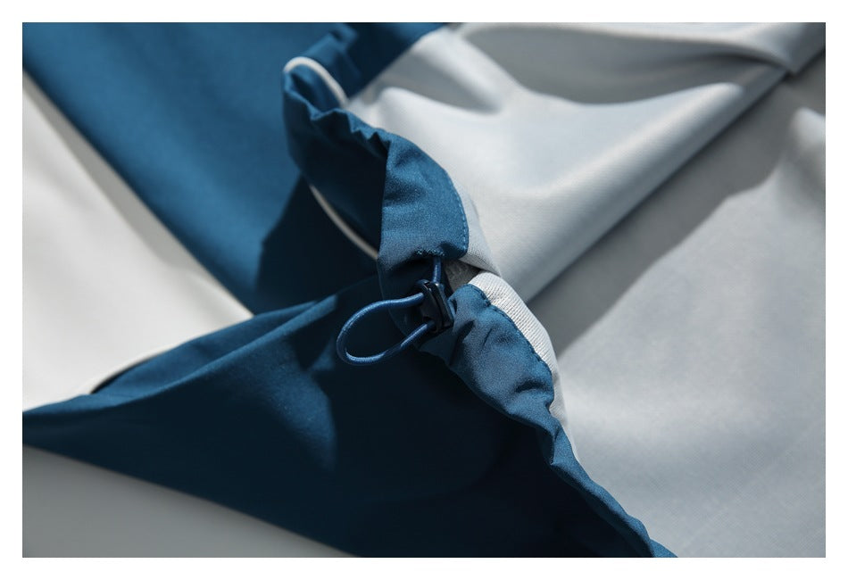 Close-up of a teal garment's adjustable drawcord and toggle beside a light-colored panel.