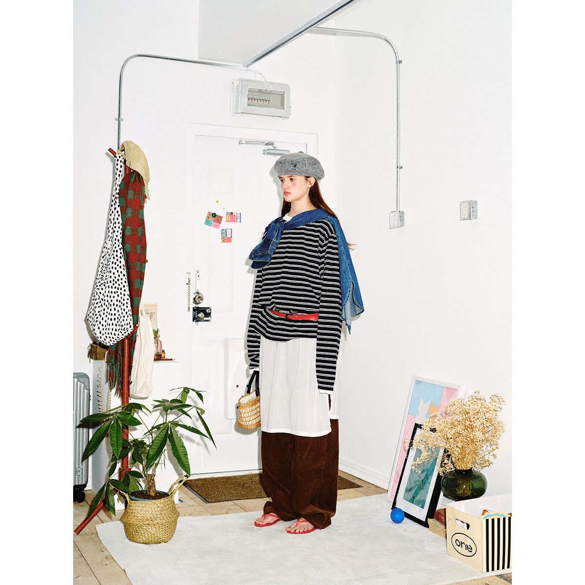 Model wearing an oversized black-and-white striped long-sleeve top, white apron-style layer, red belt and blue denim draped