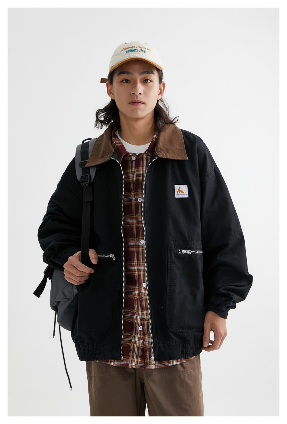 Front view of a model wearing a black jacket with a brown collar over a brown plaid shirt.