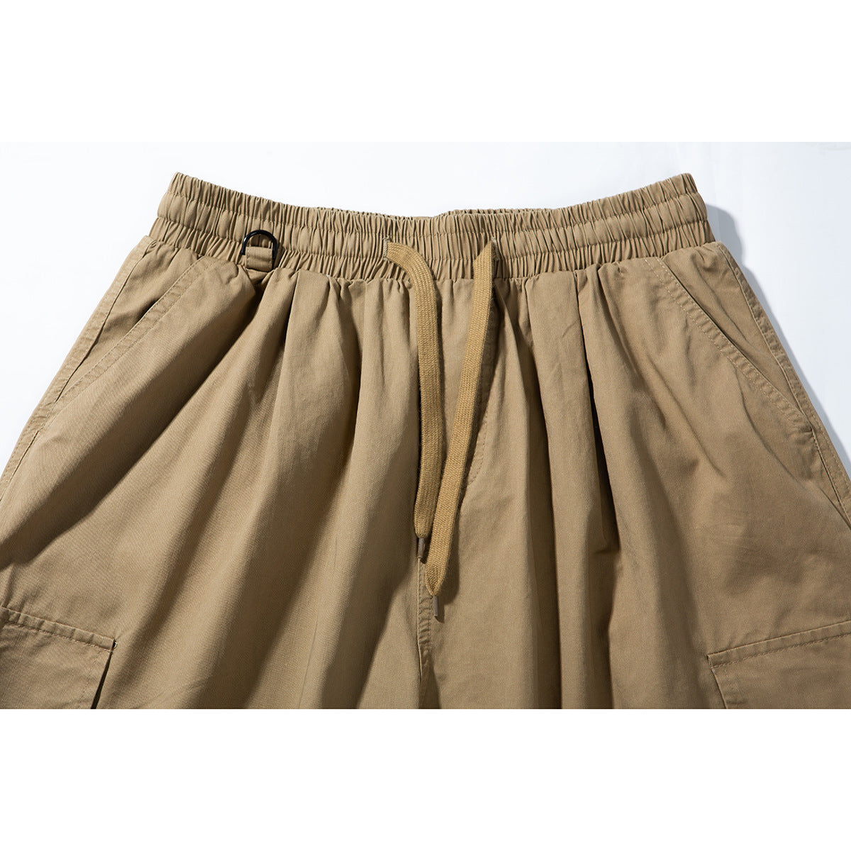 Close-up of tan shorts with a gathered elastic waistband, drawstring, side pockets and a small black loop.