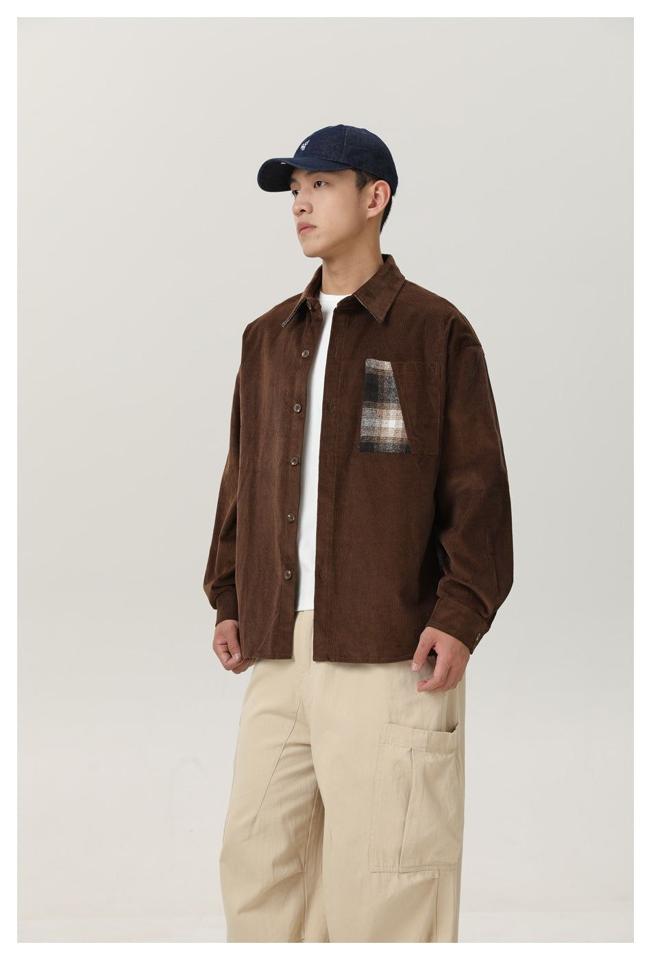 Front view of a model wearing a brown button-front shirt with a plaid chest pocket and cream cargo pants.