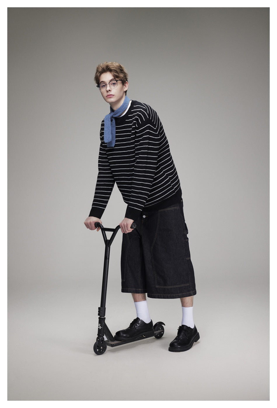 Model wearing a black sweater with white horizontal stripes, a blue scarf, and dark denim shorts.