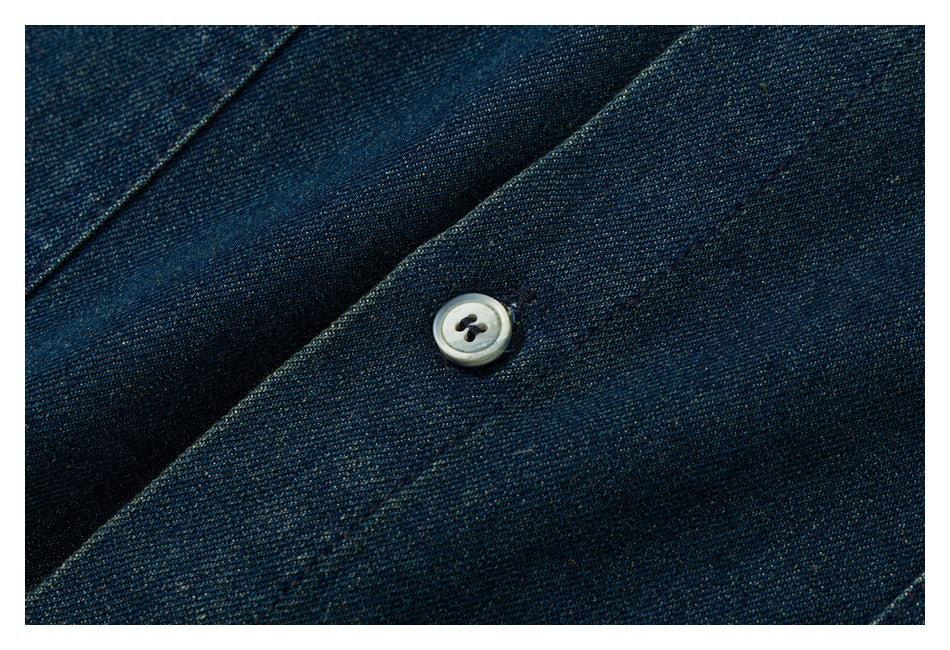 Close-up of a pale four-hole button on dark indigo denim fabric.