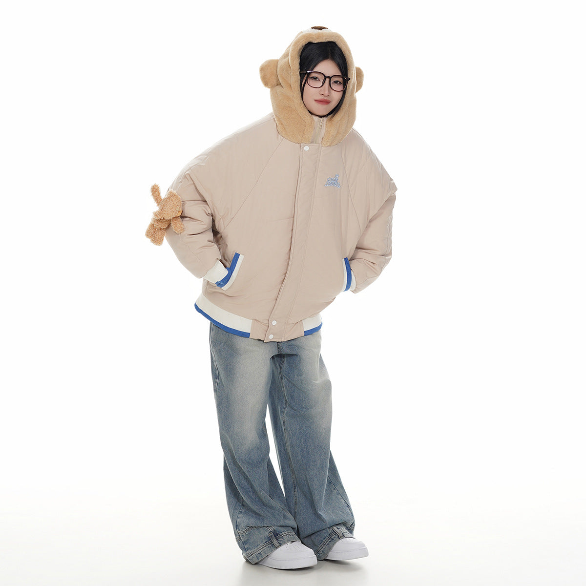 Full-length front view of a model in a beige bear-hood jacket with blue-and-white trim and wide-leg jeans.