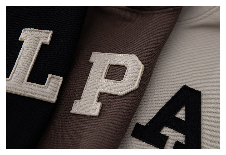 Close-up of raised varsity-style letters on black, brown, and beige garment panels.
