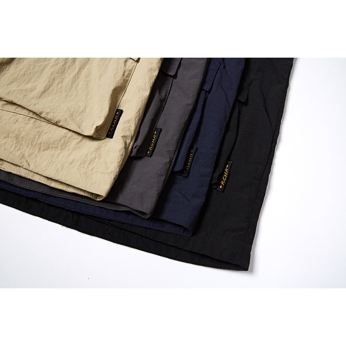 Close-up of hooded vest fabric in beige, charcoal, navy, and black, arranged in overlapping layers.