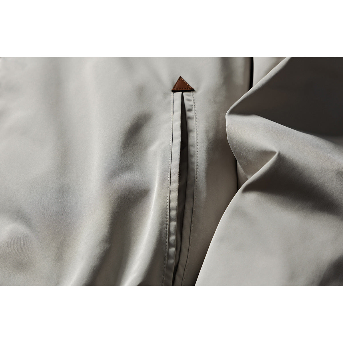 Close-up of a light gray jacket's side seam and small brown triangular fabric tab.