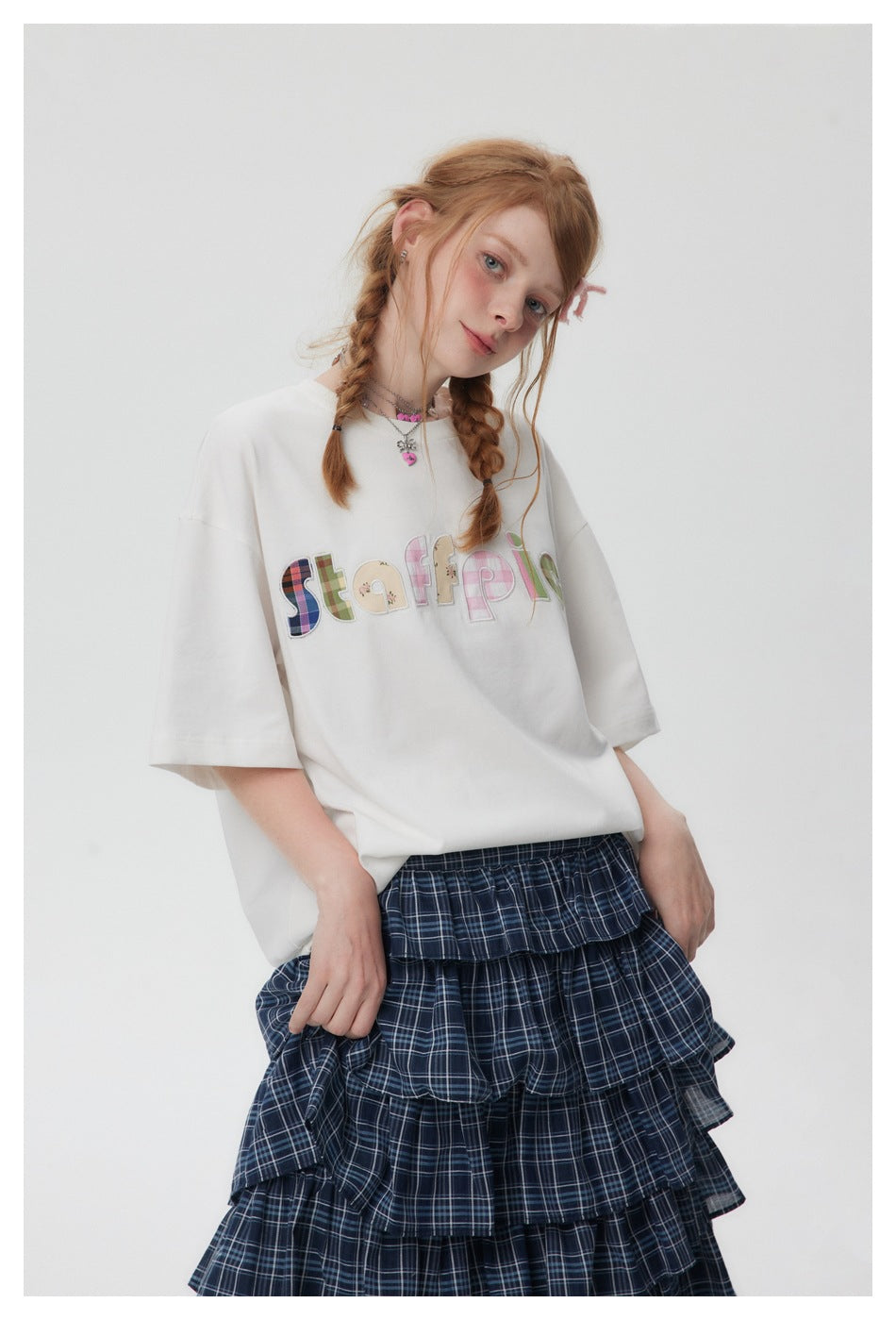 Model wearing an oversized white T-shirt with multicolored chest lettering and a navy plaid tiered skirt.