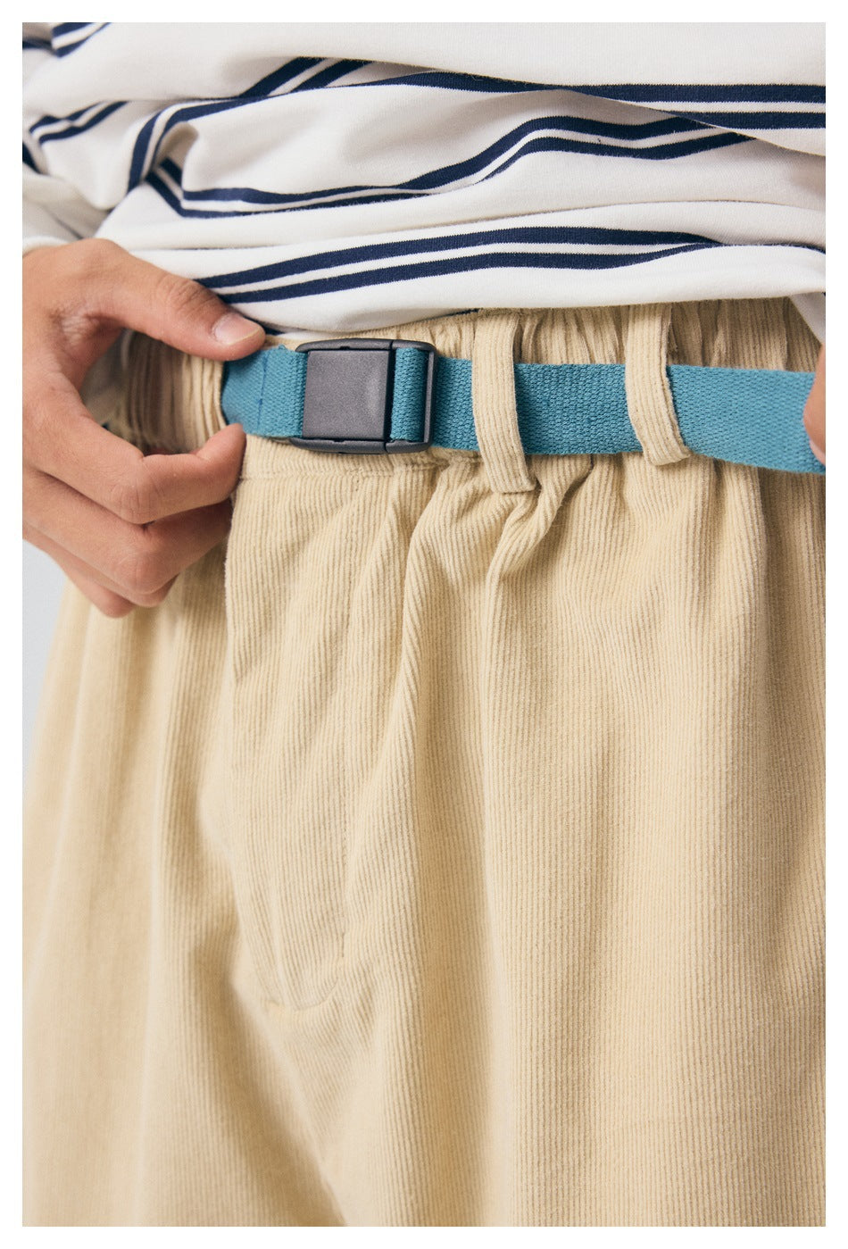Close-up of the beige pants' gathered waistband and belt loops with a blue adjustable strap and black buckle.