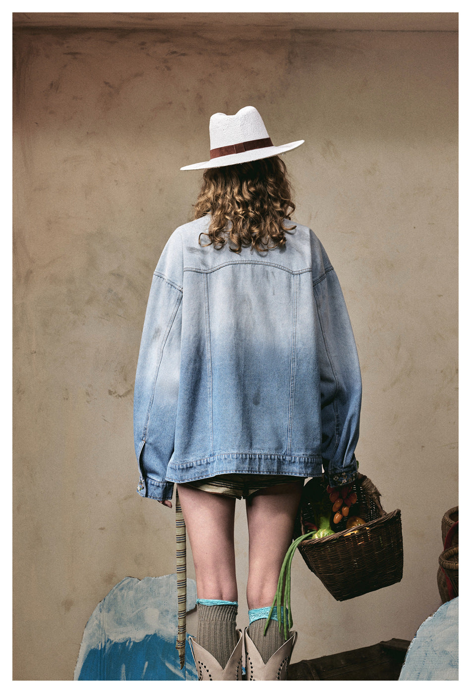 Back view of a model wearing an oversized light blue jacket with a plain back and embroidered cuffs.
